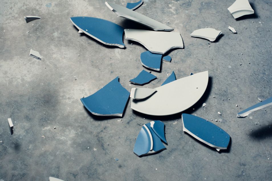 Broken pieces of blue ceramic plate on grey floor