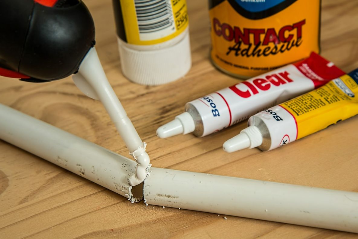 Glue is applied on a white plastic pipe with multiple types of glue laying around